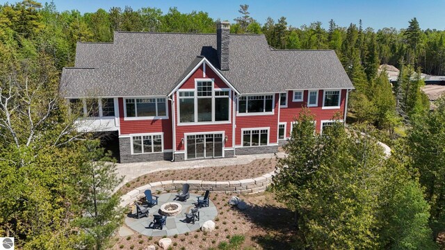 11305 Evergreen, Charlevoix, MI 49720 - rear view of property with a fire pit, a patio, a chimney, roof with shingles, and stone siding