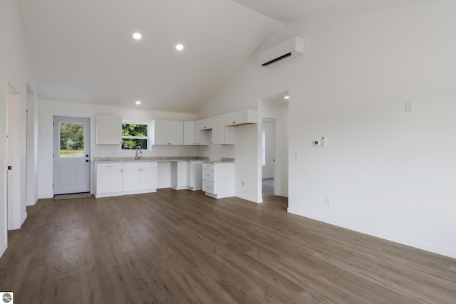 unfurnished living room with sink, high vaulted ceiling, dark hardwood / wood-style floors, and a wall unit AC