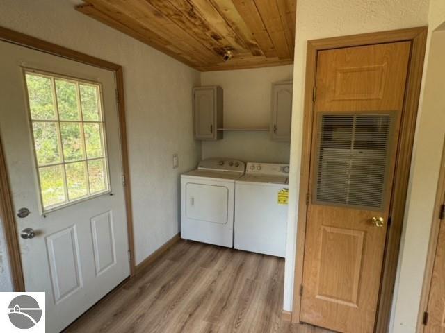 laundry room with washing machine and clothes dryer, light hardwood / wood-style floors, a healthy amount of sunlight, and cabinets