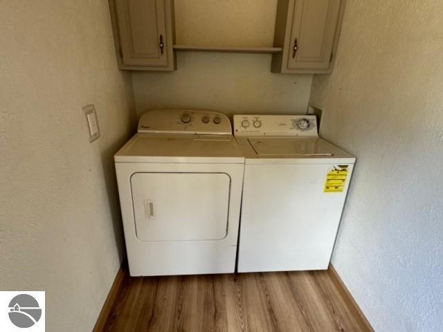 washroom featuring washing machine and clothes dryer, light hardwood / wood-style flooring, and cabinets