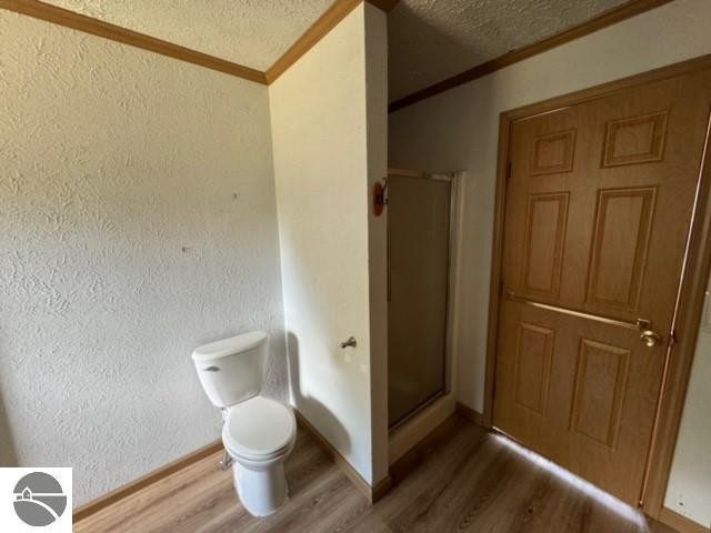 bathroom featuring ornamental molding, hardwood / wood-style flooring, a textured ceiling, toilet, and a shower with door