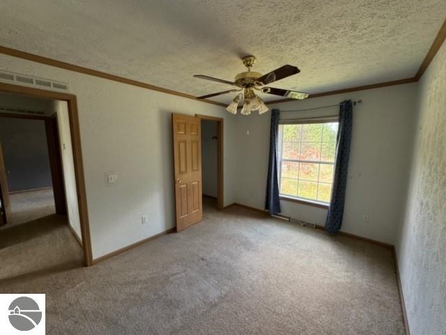 unfurnished bedroom featuring ceiling fan, carpet, a textured ceiling, and crown molding