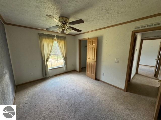 unfurnished bedroom with ceiling fan, crown molding, a textured ceiling, and carpet flooring