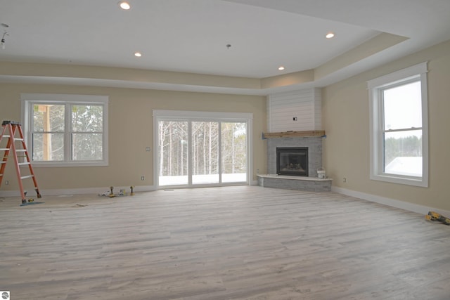 unfurnished living room with recessed lighting, a tray ceiling, baseboards, and wood finished floors