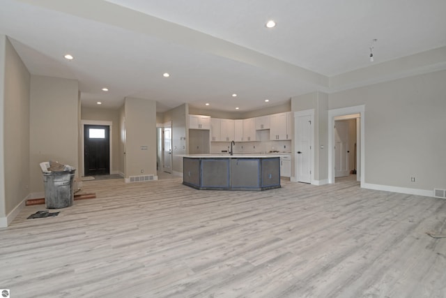 kitchen featuring light wood finished floors, recessed lighting, open floor plan, white cabinetry, and a sink