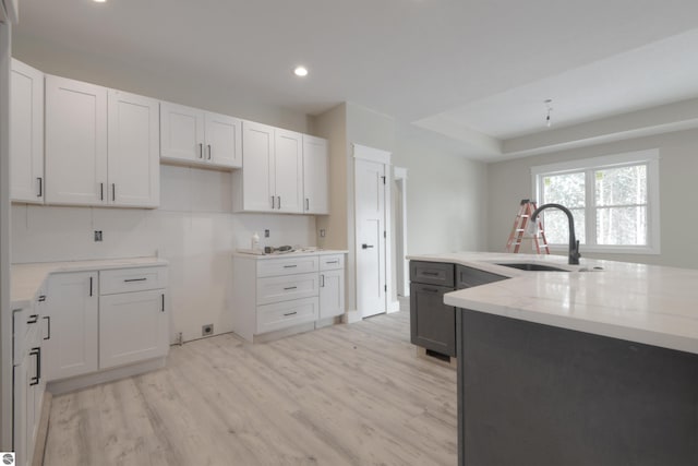 kitchen featuring light stone countertops, light wood-type flooring, white cabinetry, a sink, and recessed lighting