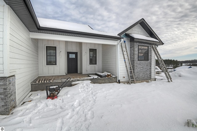 snow covered property entrance with covered porch, stone siding, and board and batten siding