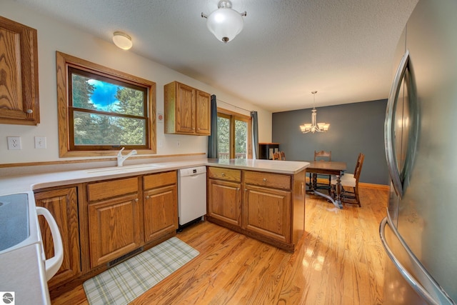 kitchen featuring stove, white dishwasher, stainless steel fridge, decorative light fixtures, and kitchen peninsula