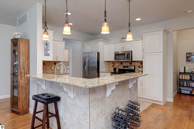 kitchen featuring light wood-type flooring, appliances with stainless steel finishes, light stone counters, and tasteful backsplash