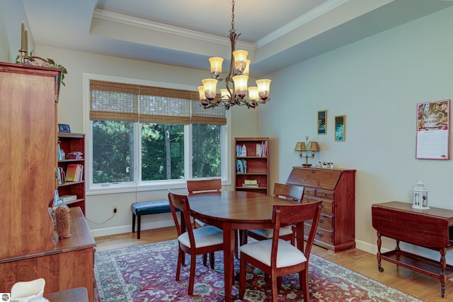 dining room with a raised ceiling, a notable chandelier, light hardwood / wood-style flooring, and ornamental molding