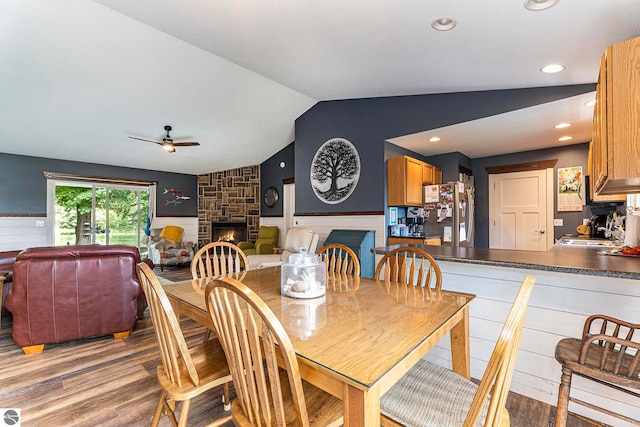 dining room with light hardwood / wood-style floors, vaulted ceiling, sink, ceiling fan, and a stone fireplace