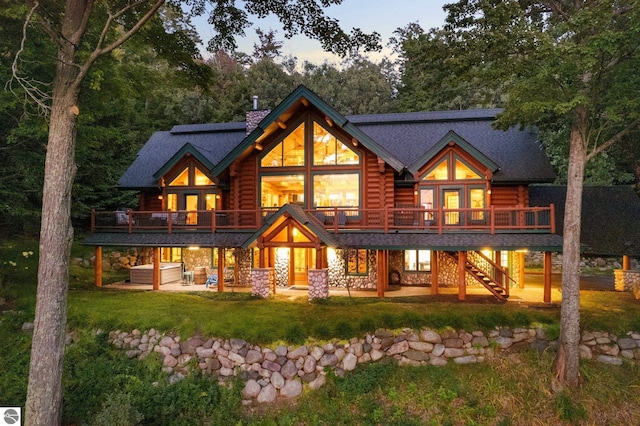 back of house at dusk featuring a patio, stone siding, french doors, log siding, and a chimney