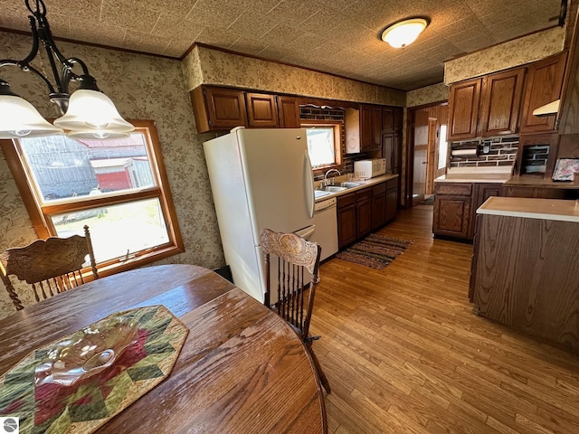 kitchen with an ornate ceiling, light wood-style floors, a sink, white appliances, and wallpapered walls