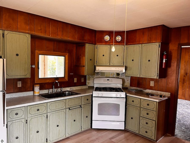 kitchen featuring sink, white gas range, light wood-type flooring, stainless steel refrigerator, and wooden walls