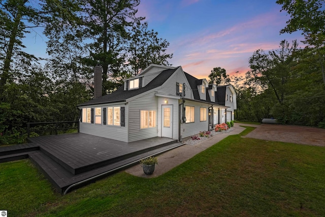 back house at dusk featuring a lawn and a wooden deck