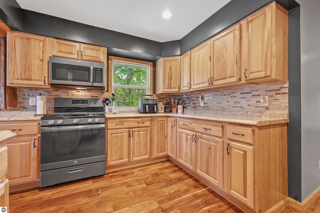 kitchen with light brown cabinets, appliances with stainless steel finishes, light wood-type flooring, and tasteful backsplash