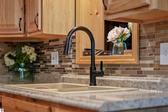 room details featuring backsplash, light stone counters, and sink