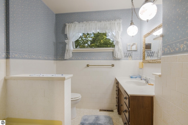 bathroom with wallpapered walls, toilet, a wainscoted wall, tile patterned floors, and vanity