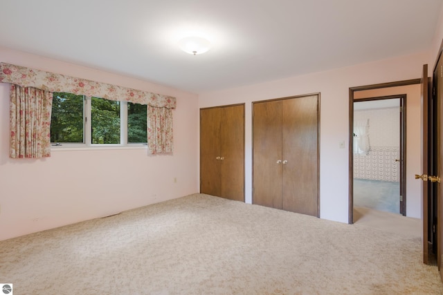 unfurnished bedroom with light colored carpet and multiple closets