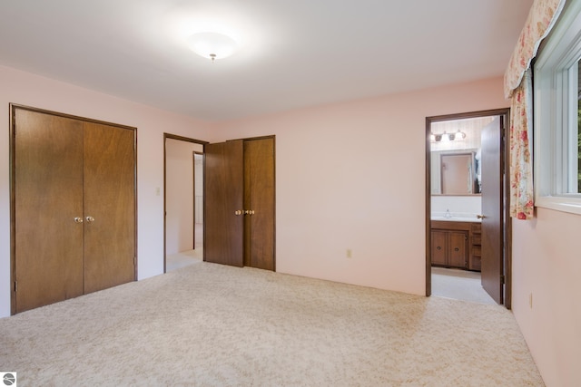 unfurnished bedroom with two closets, connected bathroom, and light colored carpet