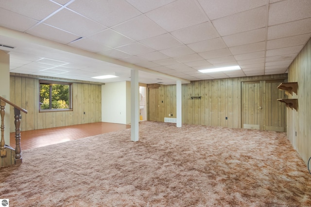 below grade area featuring a drop ceiling, wooden walls, carpet flooring, visible vents, and stairway