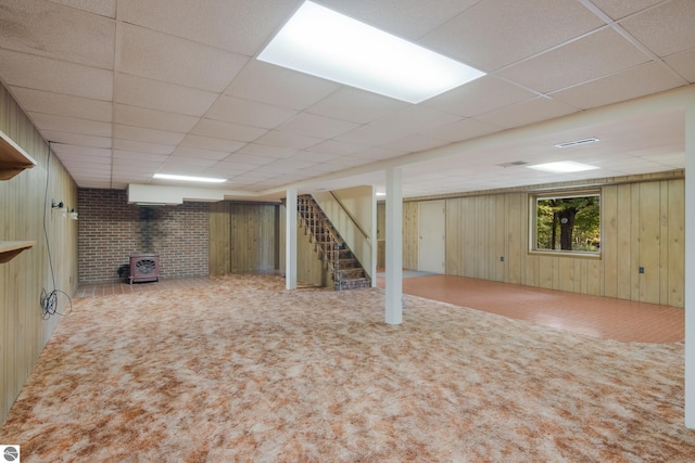 below grade area with wooden walls, a drop ceiling, a wood stove, stairs, and carpet flooring