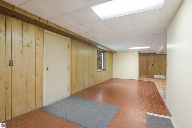 finished basement featuring brick floor, a paneled ceiling, visible vents, and wood walls