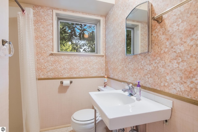 bathroom with toilet, wallpapered walls, a shower with curtain, and a wainscoted wall