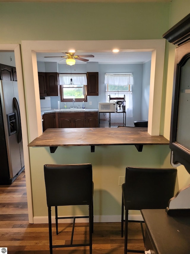 kitchen with stainless steel fridge, ceiling fan, a breakfast bar, dark hardwood / wood-style floors, and dark brown cabinetry