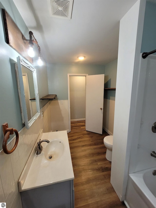 bathroom featuring toilet, vanity, wood-type flooring, decorative backsplash, and tile walls