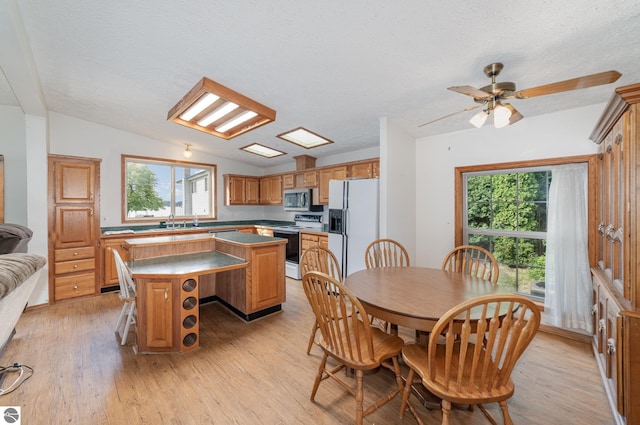 dining room featuring plenty of natural light, light wood-type flooring, vaulted ceiling, and a textured ceiling