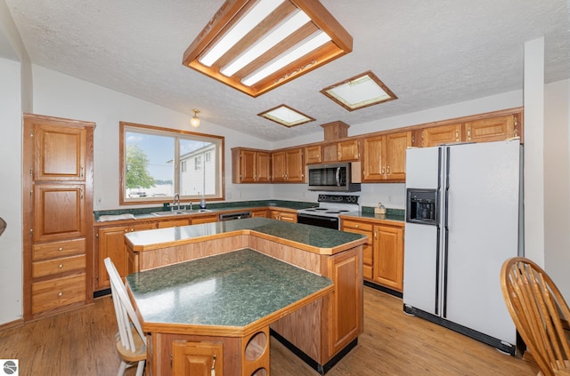 kitchen featuring white refrigerator with ice dispenser, range with electric cooktop, stainless steel microwave, a center island, and light wood-style floors