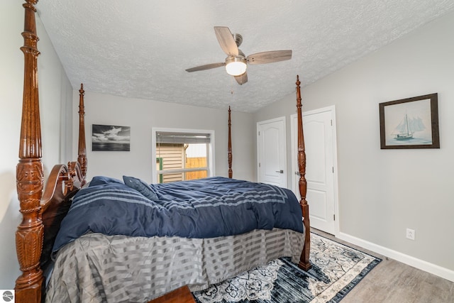 bedroom with a ceiling fan, vaulted ceiling, a textured ceiling, wood finished floors, and baseboards