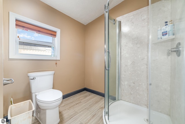 full bathroom featuring baseboards, toilet, wood finished floors, a textured ceiling, and a shower stall