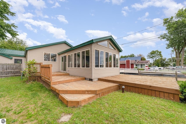 rear view of property featuring a lawn, a wooden deck, a sunroom, and fence