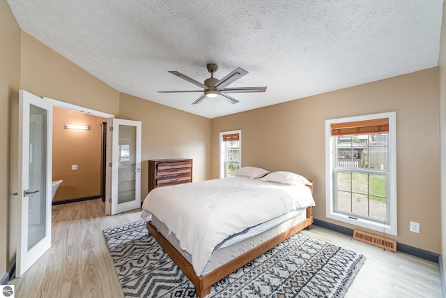 bedroom featuring lofted ceiling, multiple windows, light wood-type flooring, and visible vents