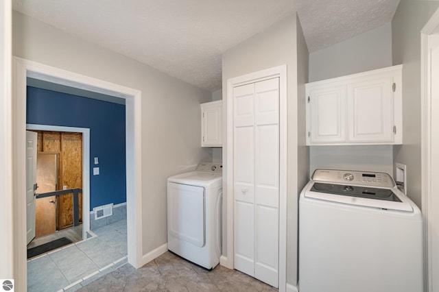 clothes washing area with washer and dryer, cabinet space, visible vents, and a textured ceiling