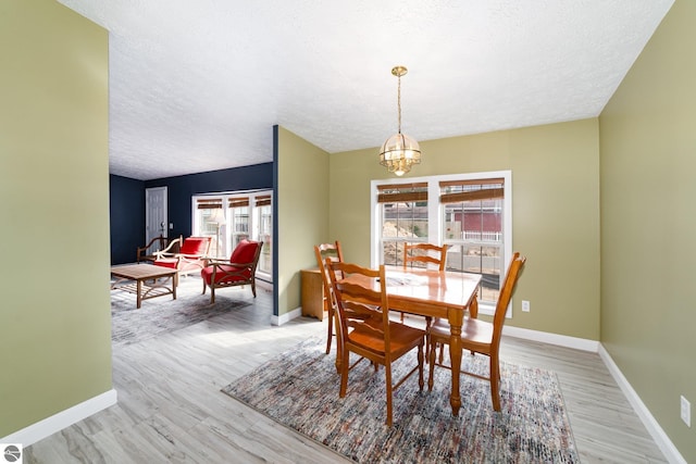 dining area with baseboards, light wood-style floors, a textured ceiling, and an inviting chandelier