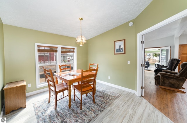 dining area with light wood-type flooring, lofted ceiling, a notable chandelier, and a textured ceiling