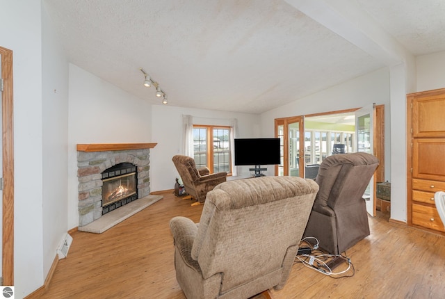 living area with lofted ceiling with beams, a textured ceiling, light wood-style floors, a fireplace, and a wealth of natural light