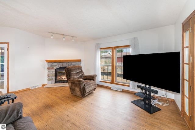 living area with visible vents, a stone fireplace, a textured ceiling, and wood finished floors