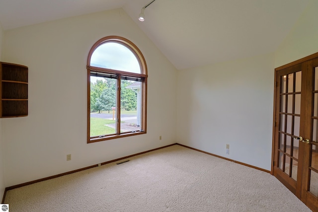 carpeted empty room with lofted ceiling and rail lighting