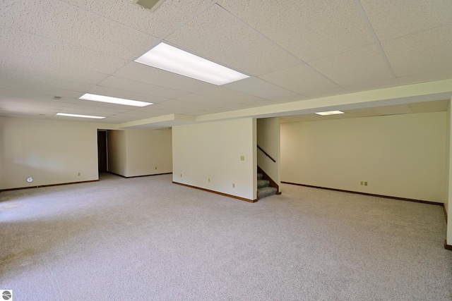 finished below grade area featuring a drop ceiling, light colored carpet, stairs, and baseboards