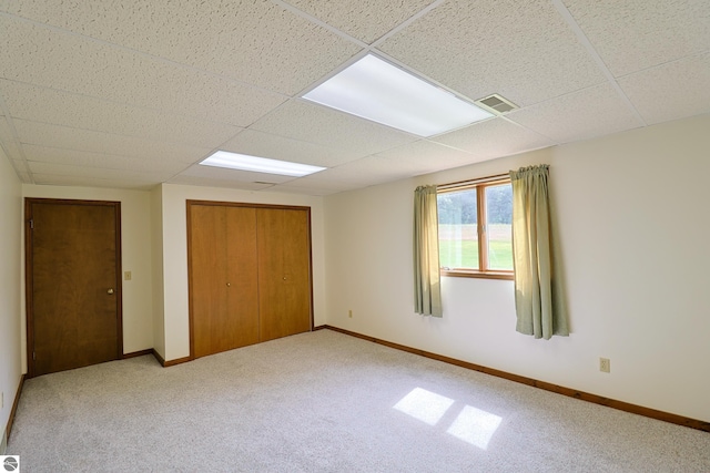 unfurnished bedroom with visible vents, carpet floors, baseboards, a paneled ceiling, and a closet