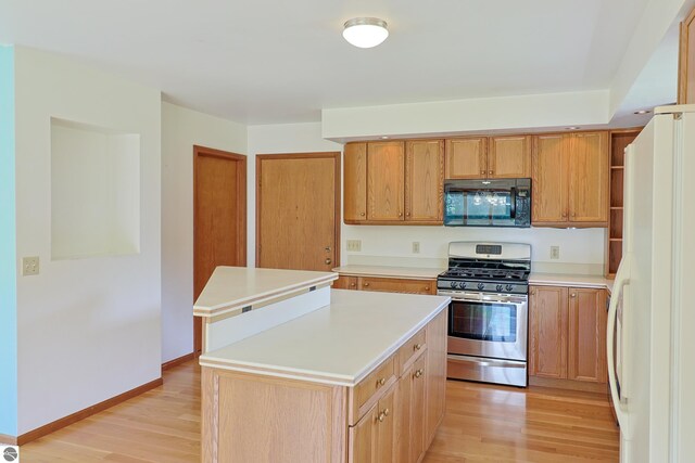 kitchen with stainless steel range with gas stovetop, freestanding refrigerator, light countertops, light wood-style floors, and black microwave