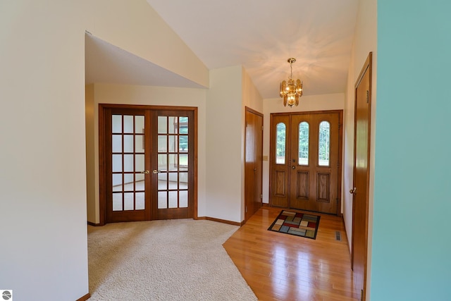 foyer featuring lofted ceiling, wood-type flooring, a notable chandelier, and french doors