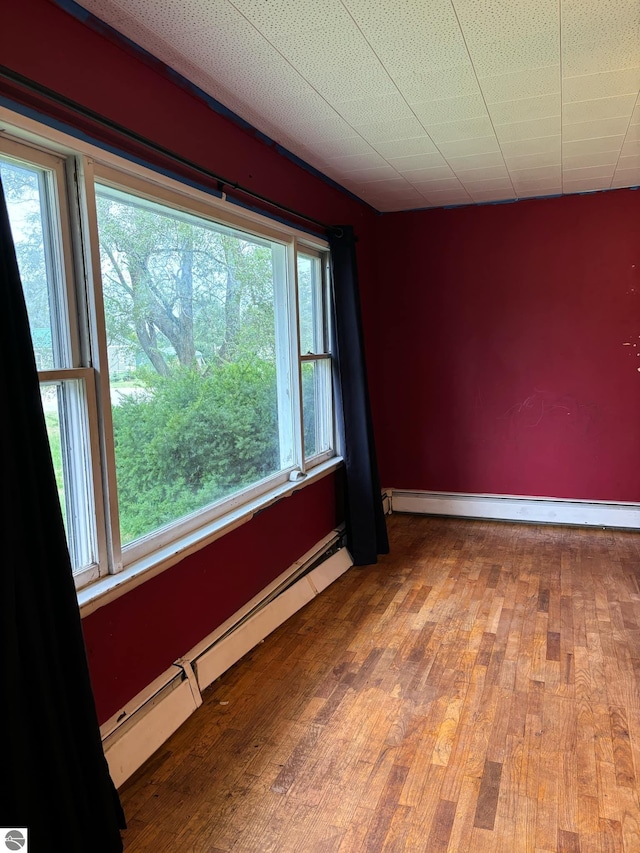 spare room with wood-type flooring, a wealth of natural light, and a baseboard heating unit