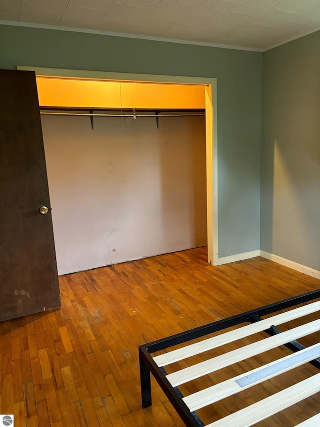 unfurnished bedroom featuring wood-type flooring, a textured ceiling, a closet, and ornamental molding