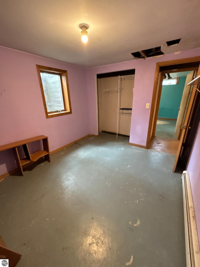 unfurnished bedroom featuring concrete floors, baseboard heating, and a closet