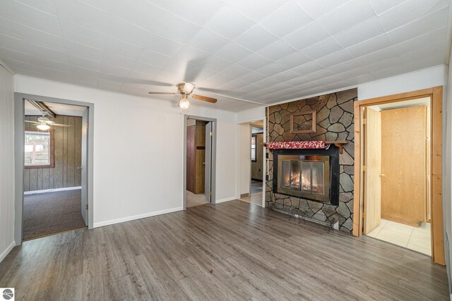 unfurnished living room featuring a fireplace, hardwood / wood-style flooring, wood walls, and ceiling fan